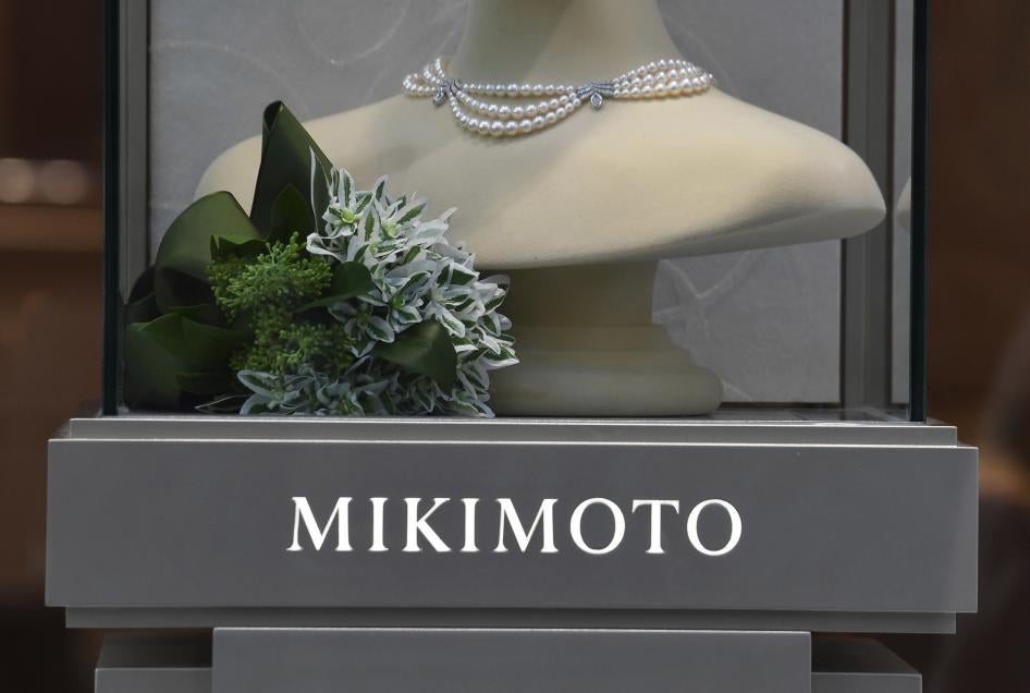 A pearl necklace is displayed over a gray sign that reads "Mikimoto"