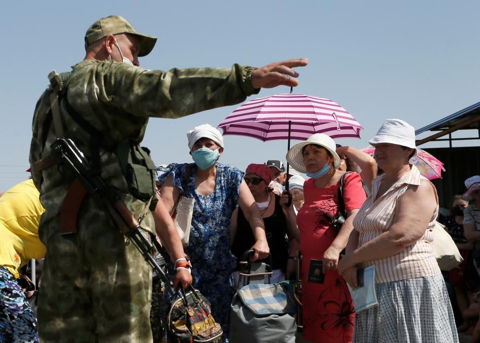 Люди слушают вооруженного человека из так называемой "ДНР" во время ожидания перед пересечением линии соприкосновения на контрольно-пропускном пункте, который был временно закрыт в связи с пандемией Covid-19, а затем вновь открыт, возле поселка Оленевка Донецкой области, Украина, 7 июля 2020 года.