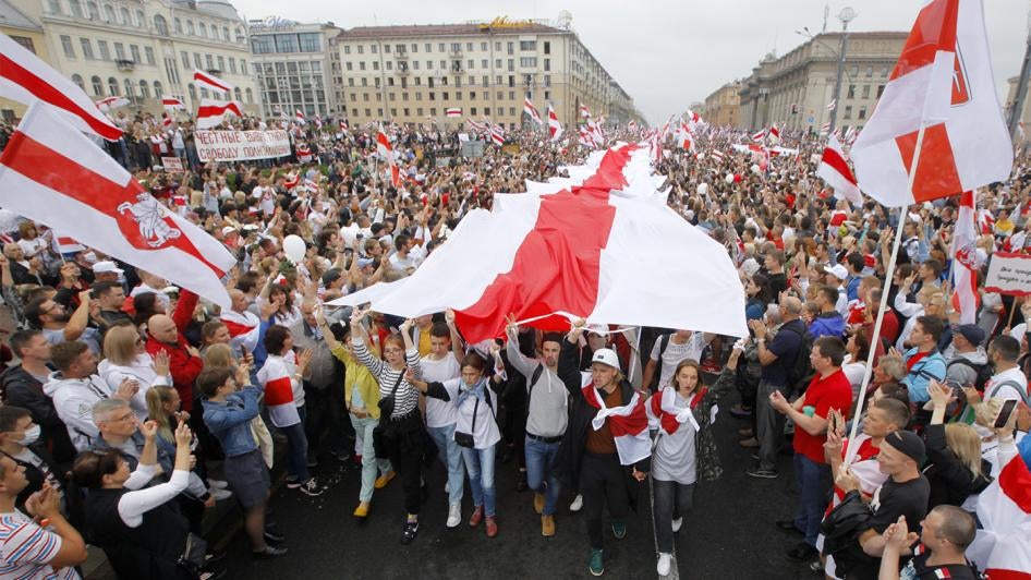 Демонстранты несут большой исторический флаг Беларуси. 23 августа 2020 г. тысячи людей вышли на протест на площади Независимости в Минске, Беларусь.