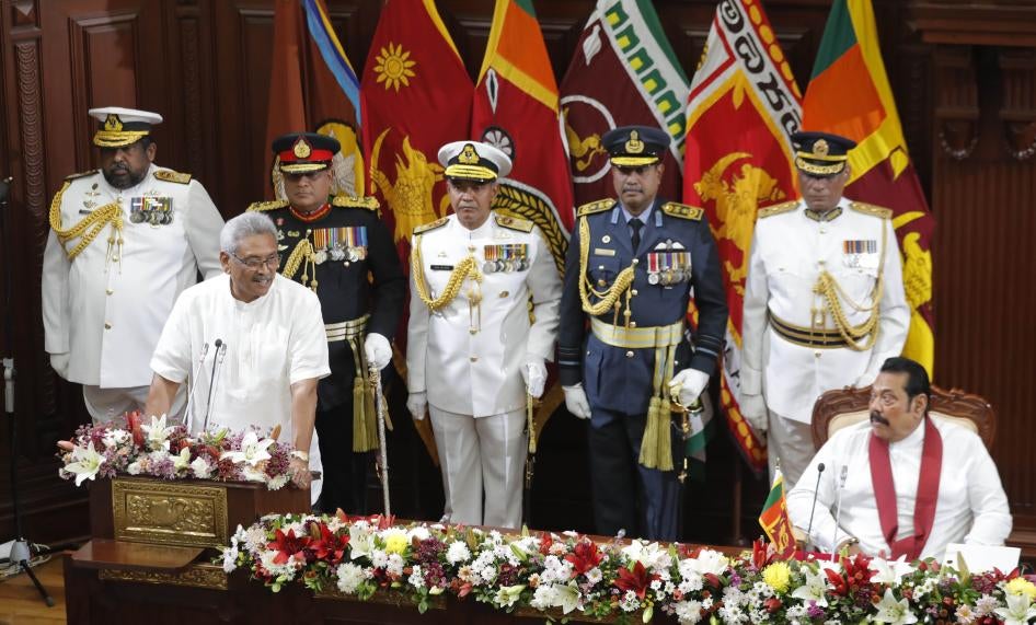 A man in white stands at a podium in front of uniformed military officers