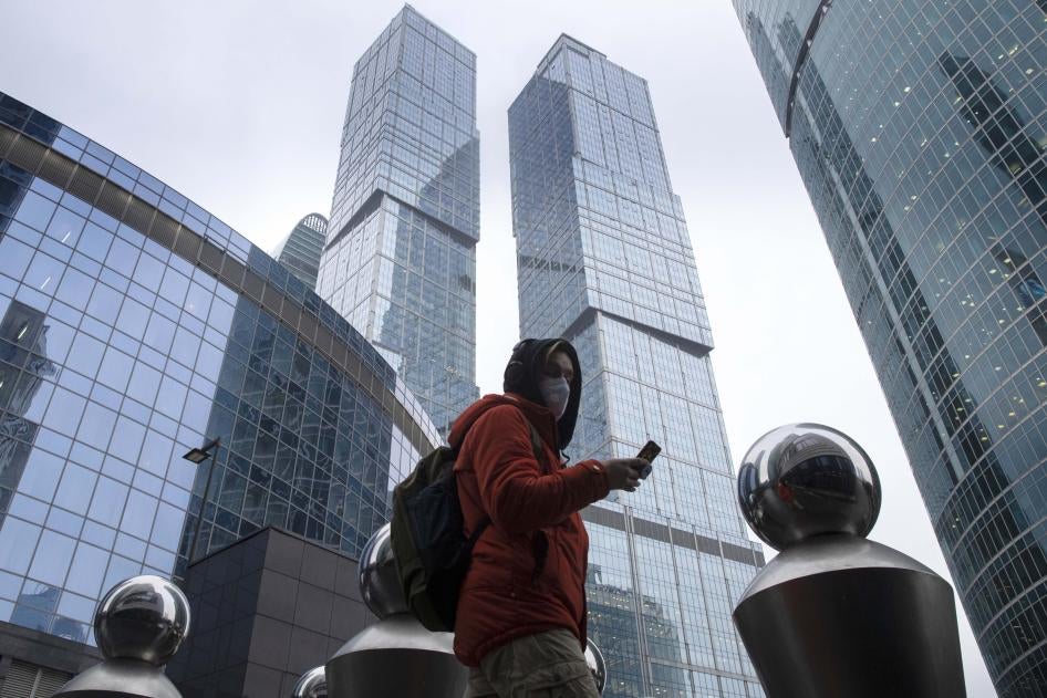 A man wearing a face mask to protect against Covid-19 uses his smartphone among Moscow City skyscrapers in Moscow, Russia, January 11, 2021.