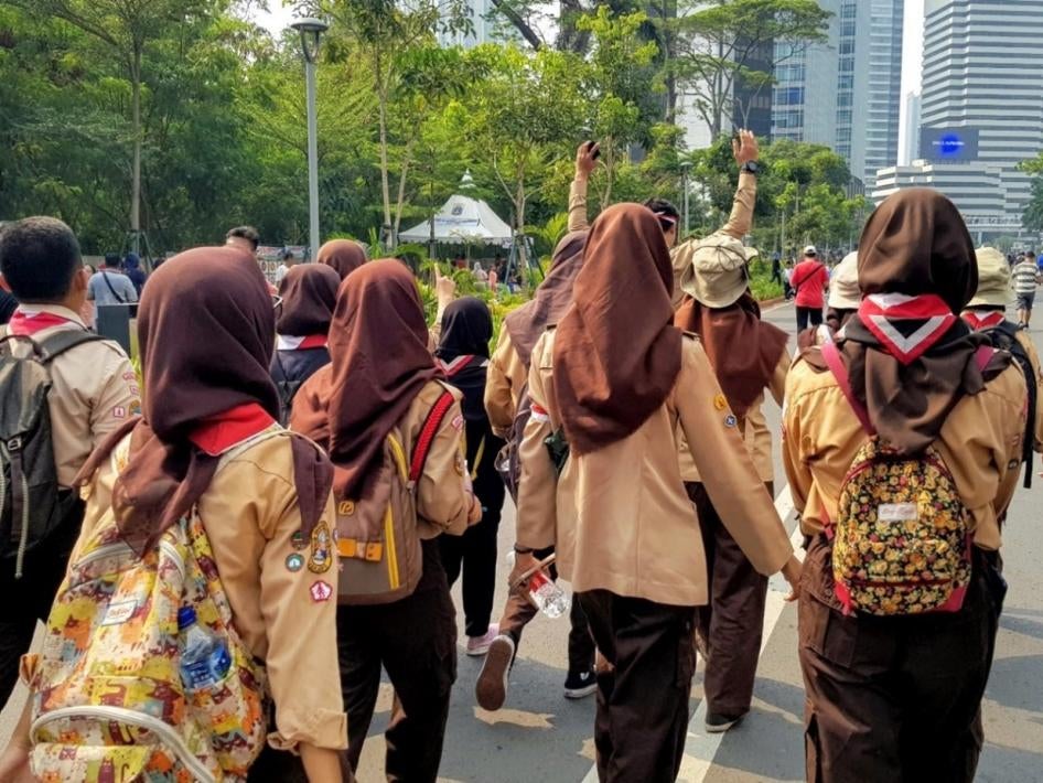 A group of girls wearing brown hijabs and backpacks walk down the street