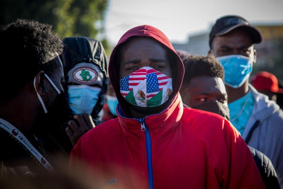 A migrant from Haiti wearing a mask in the colors of the Mexican and US flags stands at a border crossing with others, waiting to asylum in the US, February 19, 2021. 