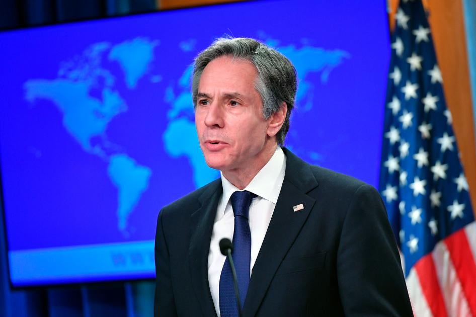 Secretary of State Antony Blinken speaks at the State Department in Washington, standing in front of a world map and a US flag.