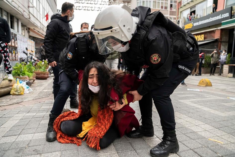 Police forcefully detain a protester  who is crying on the ground while the police stand over her at a demonstration. 