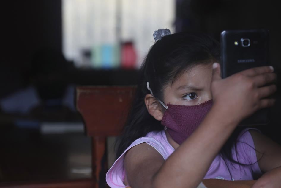Una niña con mascarilla usa un teléfono para poder asistir a las clases en línea. 