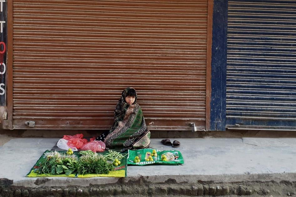 Une fillette népalaise assise devant un étalage de légumes et de fruits disponibles à la vente et posés par terre sur deux sacs d’emballage, dans une rue de Katmandou, au Népal, le 12 juin 2020. Derrière elle, le magasin était fermé en raison de la pandémie de Covid-19. 
