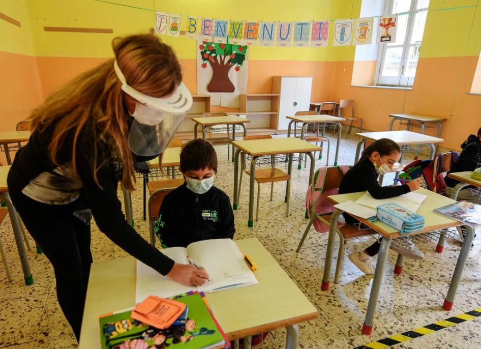 Un'insegnante aiuta alcuni bambini seduti in una classe vuota. Tutti portano mascherine sul viso.
