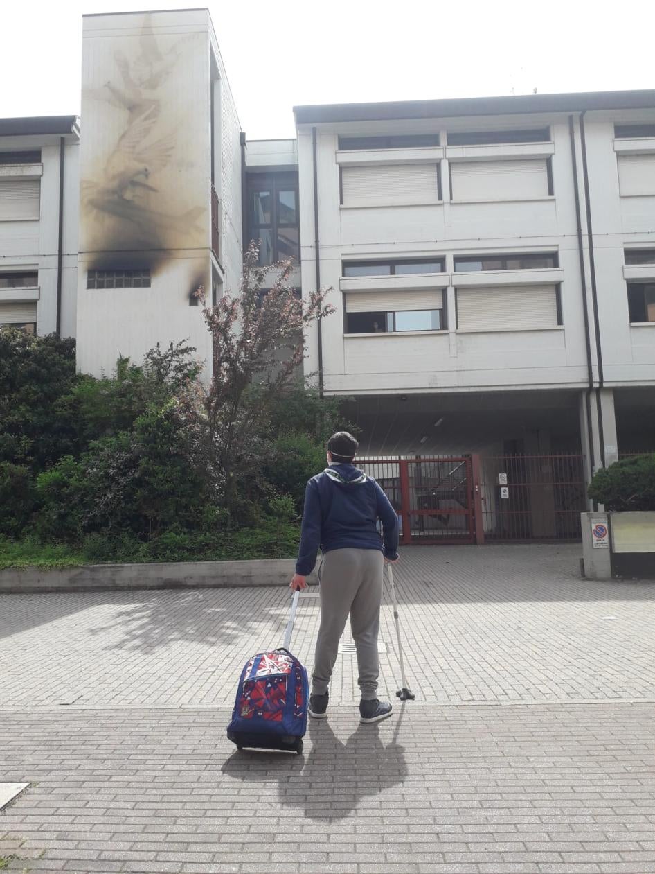 Un ragazzo con uno zaino cammina con un bastone dirigendosi verso un edificio.