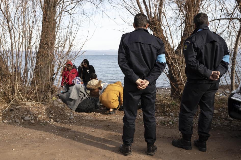 Frontex border officers stand near migrants on the island of Lesbos, Greece, on March 2020.