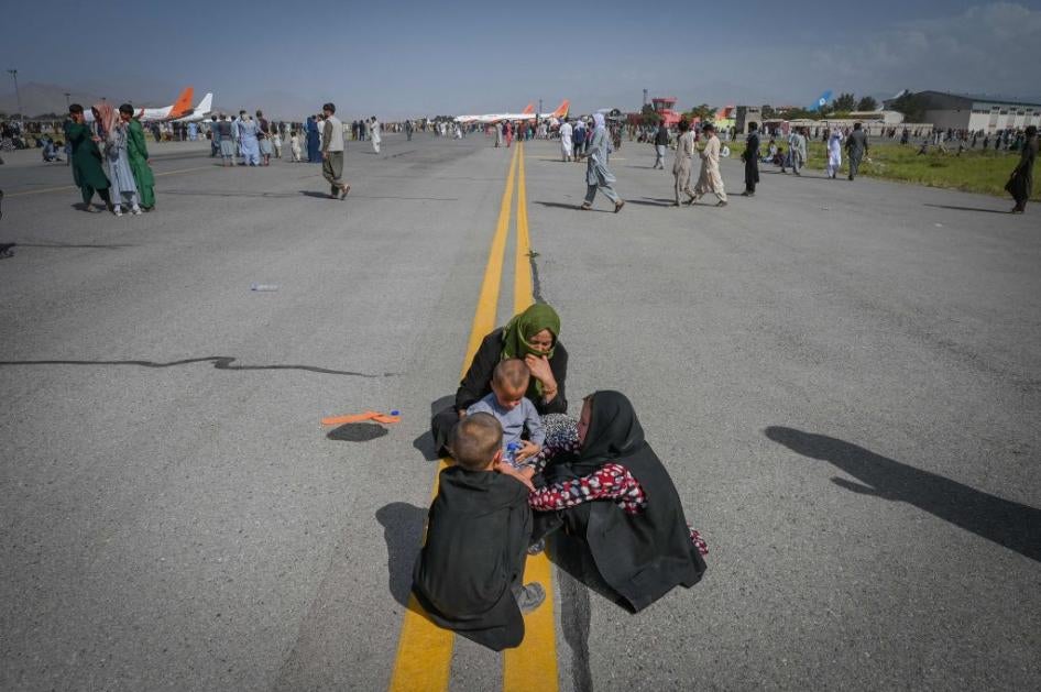 Several Afghans sit on the tarmac awaiting to leave from Kabul's airport on August 16, 2021.