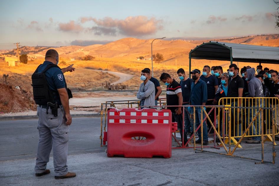 Palestinian laborers line up to cross a checkpoint at the entrance to the Israeli settlement of Maale Adumim, near Jerusalem, June 30, 2020. 