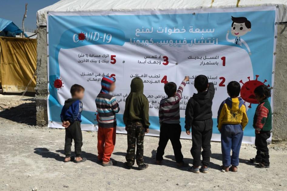 Displaced Syrian children read a poster, outlining 7 steps to prevent the spread of COVID-19 coronavirus disease, at a camp for the internally displaced near Dayr Ballut, near the Turkish border in the rebel-held part of Aleppo province on March 22, 2020, during a campaign to prevent the spread of the virus.