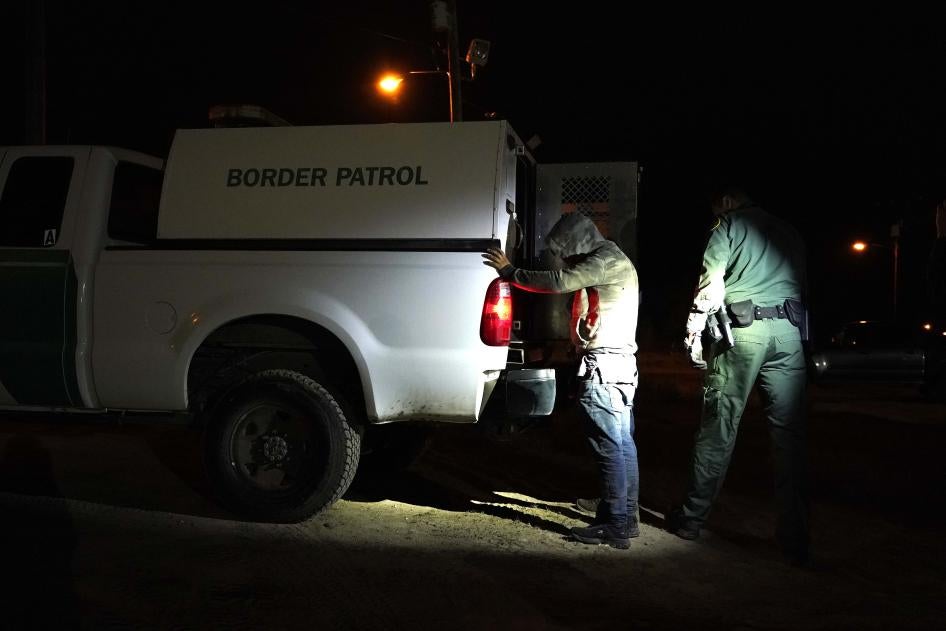 A man stands with his hands on the back of a van marked "Border Patrol"