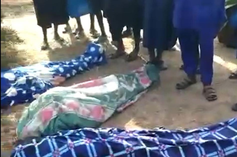 People stand over three bodies wrapped in fabric