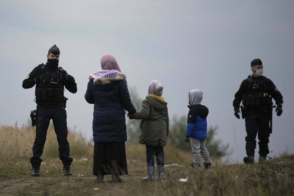 Une femme et deux enfants se tiennent devant deux policiers.
