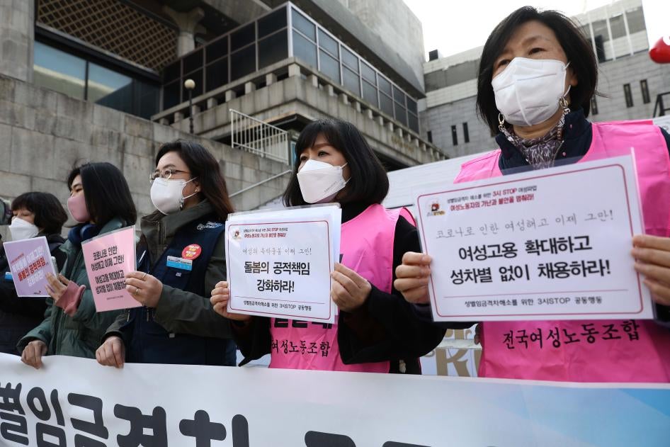 南韓社運人士在國際婦女節遊行中舉起抗議歧視婦女的標語，南韓首爾，2021年3月8日。右側標語說：「擴大女性就業，反對就業性別歧視」，中間的說：「強化公共照顧[兒童]責任」。