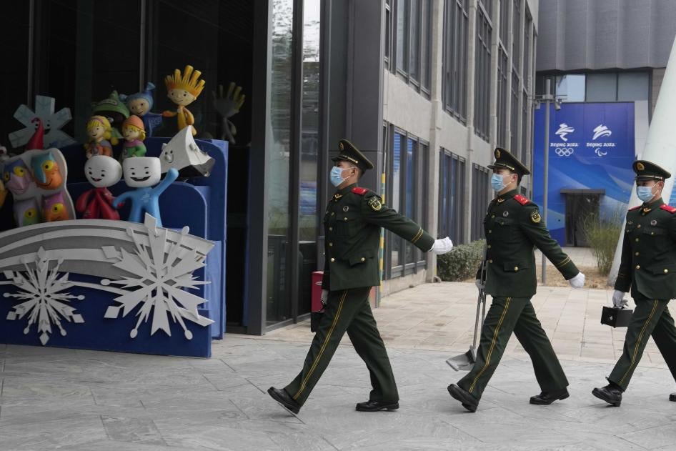 Des membres d’une unité de police paramilitaire chinoise marchaient près de mascottes de précédents Jeux olympiques d'hiver, exposées au parc Shougang à Pékin, le 21 janvier 2022. 