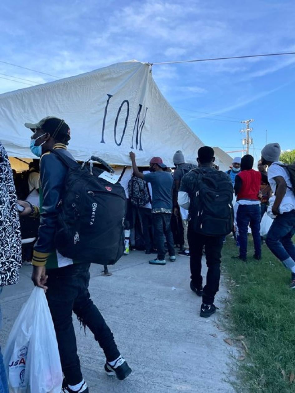 Personas expulsadas o deportadas de Estados Unidos se reúnen alrededor de una carpa de la OIM en el aeropuerto de Puerto Príncipe, en diciembre de 2021.