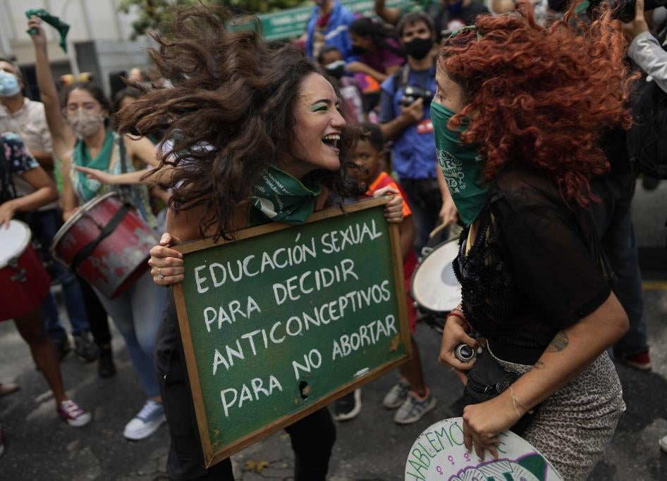 Dos mujeres saltan y sonríen mientras sostienen un cartel de protesta