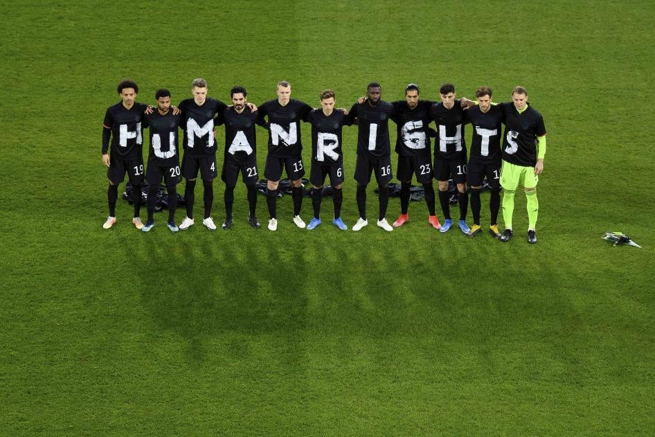 Soccer players stand in a line wearing shirts that spell out "HUMAN RIGHTS"