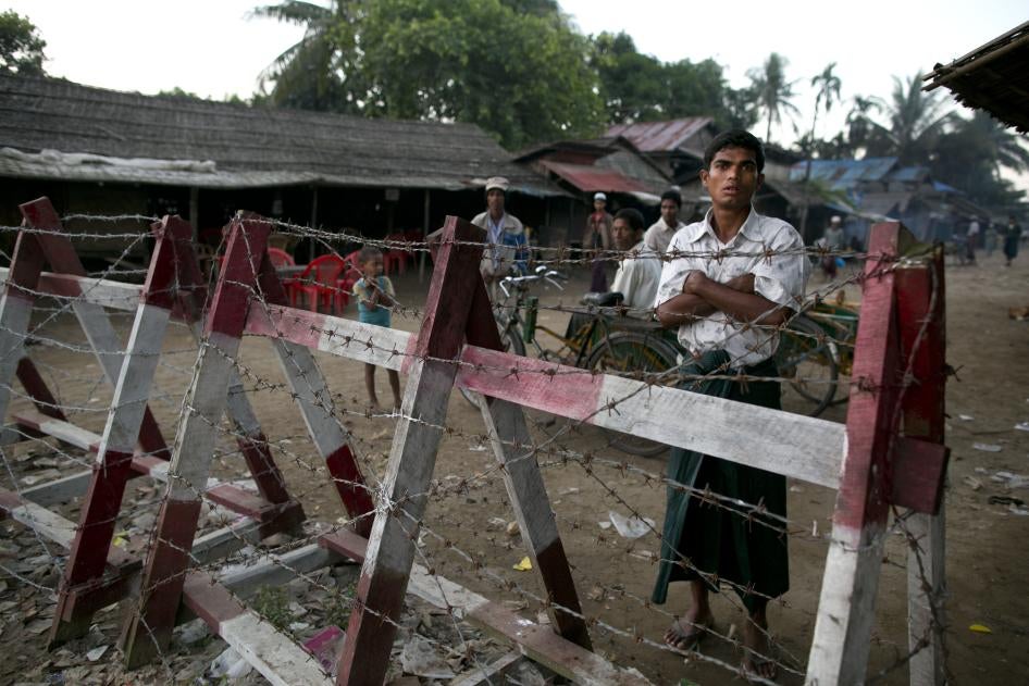 A Rohingya man looks out from a barbed wire fence