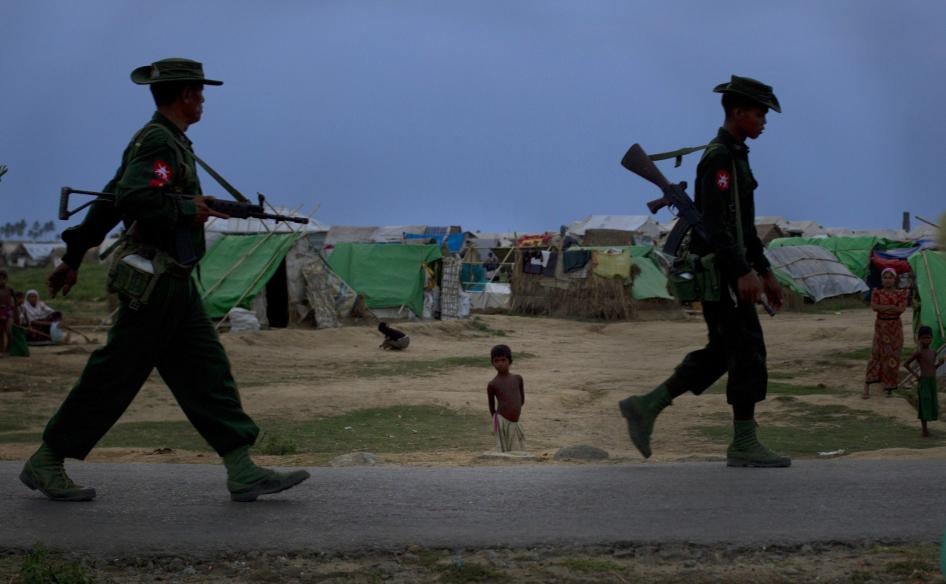 Deux soldats myanmarais passaient devant un jeune garçon rohingya dans un camp situé dans la banlieue de Sittwe, la capitale de l’État de Rakhine, dans l’ouest du Myanmar, en mai 2013.