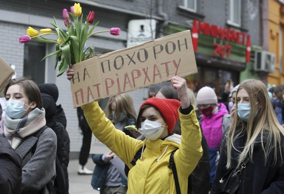 A woman carries flowers and a placard that says "At the funeral of the patriarchy" during the feminist's Women March