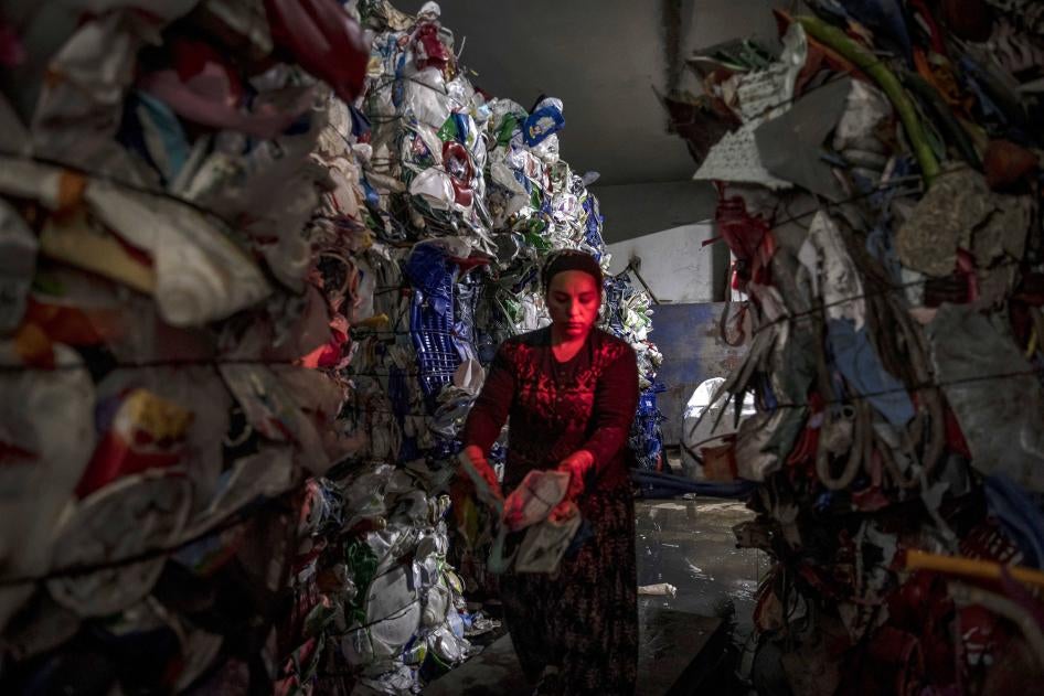 A woman stands between piles of plastic