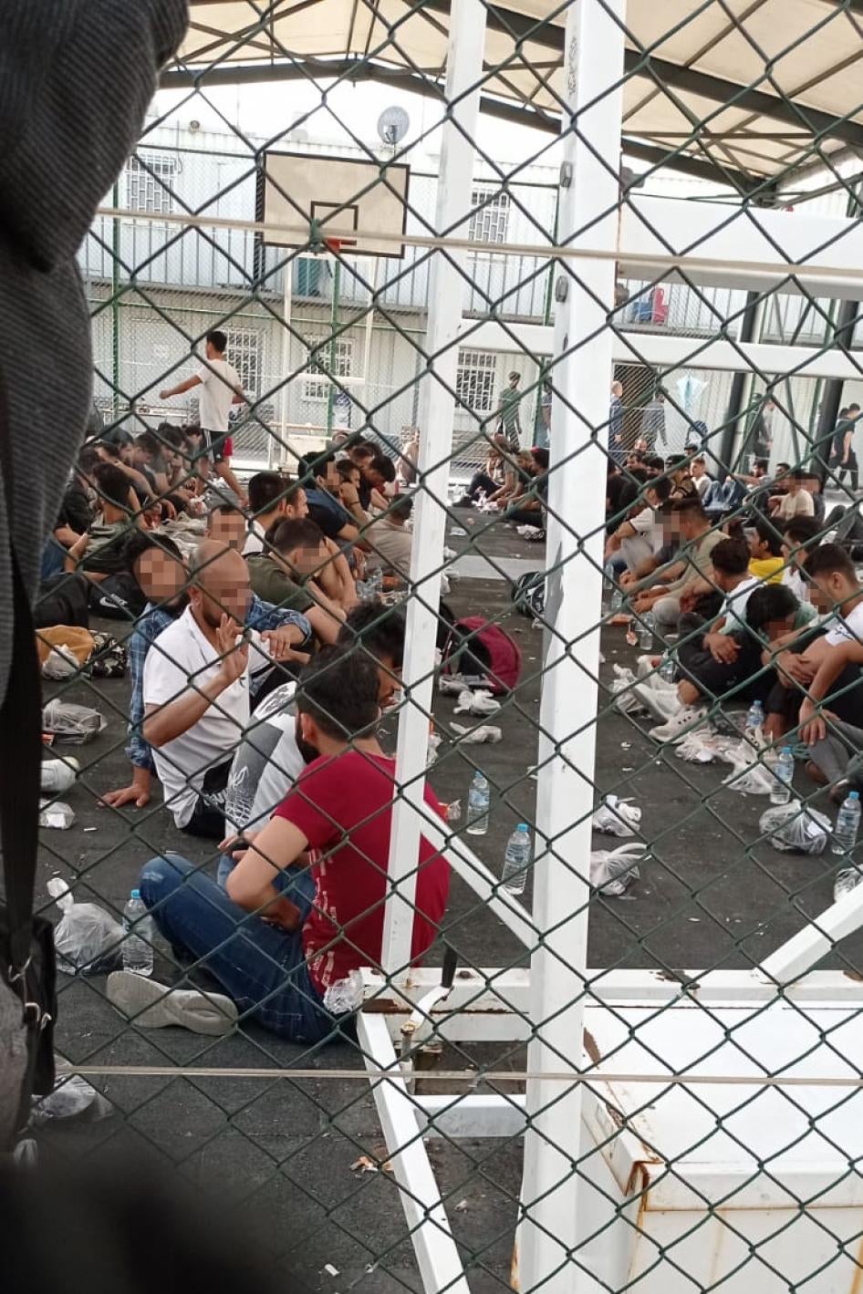 مهاجرون ولاجئون محتجزون في ملعب لكرة السلة لساعات أثناء انتظار زنزانة في مركز الإبعاد في توزلا في يونيو/حزيران 2022.  © 2022 خاص