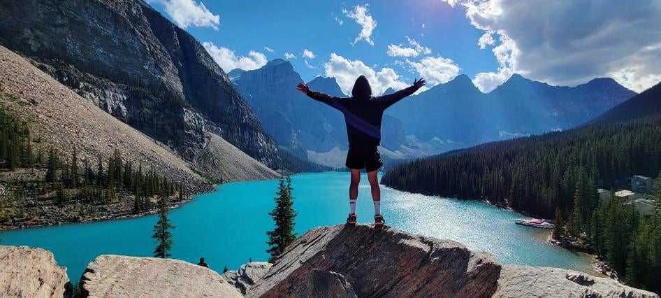 Walid standing with arms stretched at Moraine Lake in Banff.