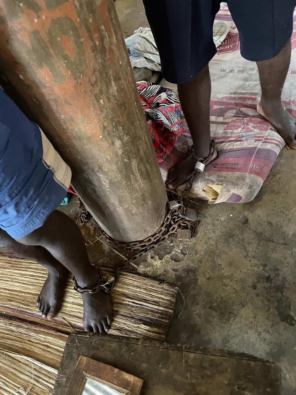 Two men are shown having one of their ankles chained to a log-like structure.