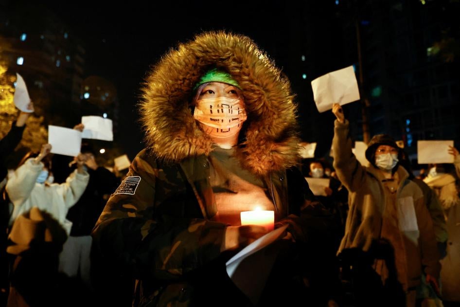 People gather in Beijing for a vigil and hold candles and white sheets of paper in protest of Covid-19 restrictions.
