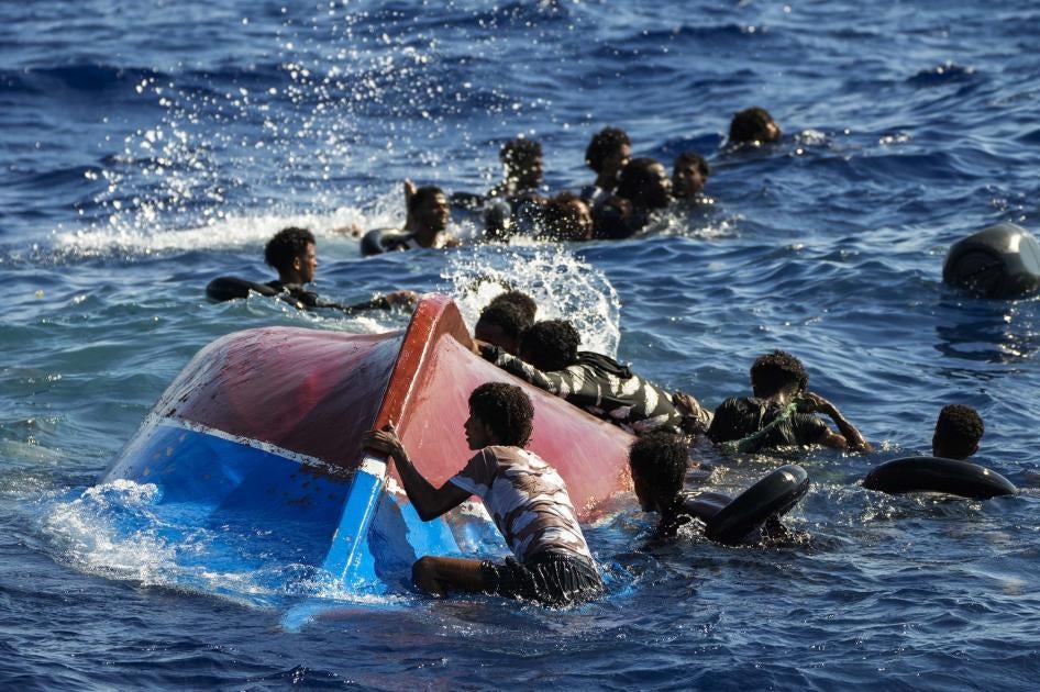 Alcuni migranti nuotano accanto alla loro barca di legno rovesciata mentre l'ONG spagnola Open Arms esegue un'operazione di soccorso per salvarli, a sud dell'isola italiana di Lampedusa nel Mar Mediterraneo, 11 agosto 2022.