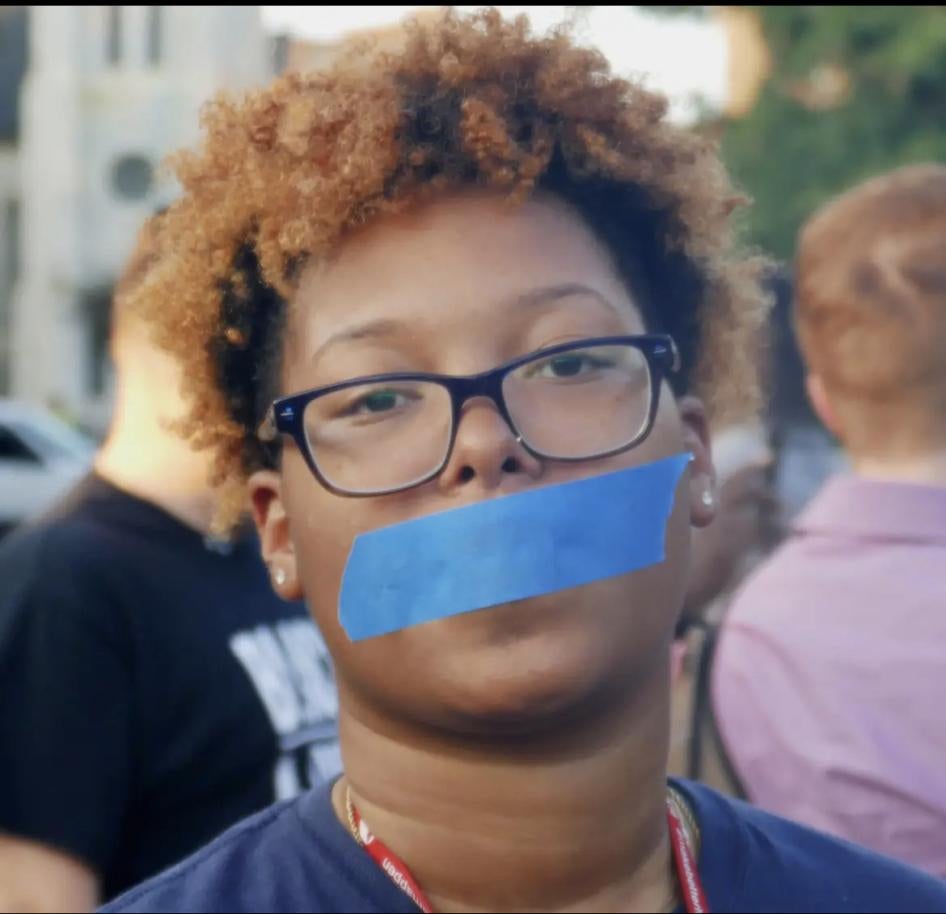 An activist with tape over their mouths