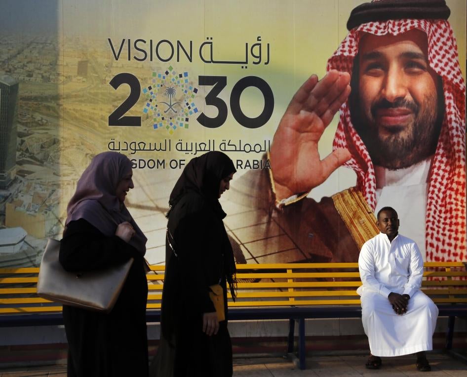أشخاص يسيرون بجانب لافتة "رؤية 2030" تُظهر ولي العهد السعودي محمد بن سلمان في جدة.