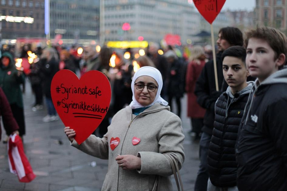 Syrian refugees hold a protest sign that reads "Syria Not Safe"