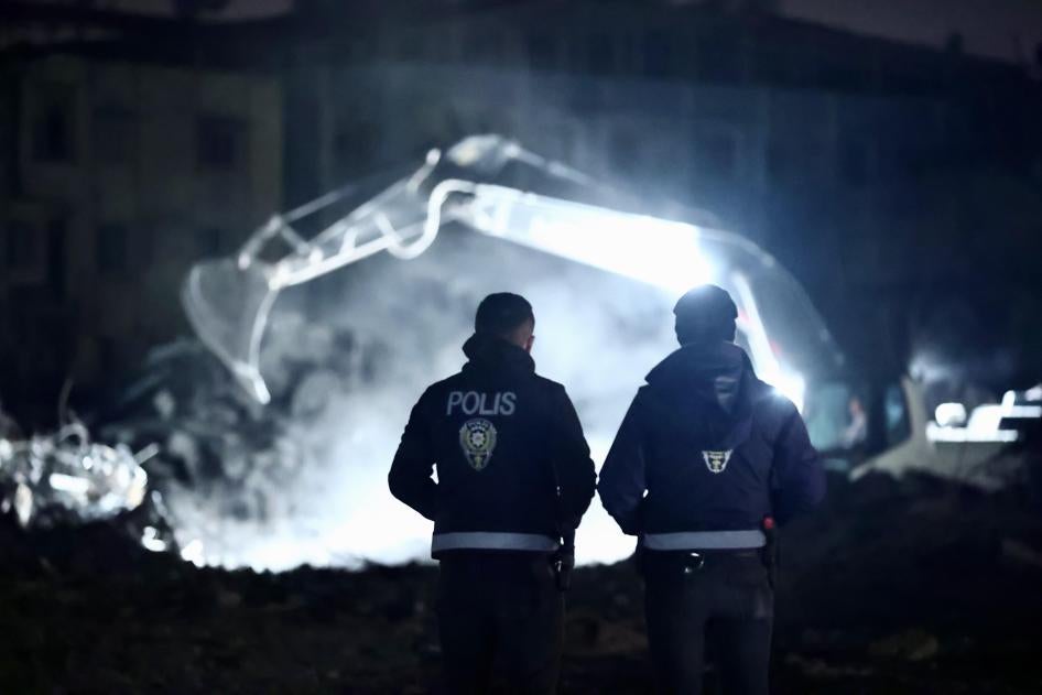 İki polis memuru, 6 Şubat depremlerinde yıkılan binaların enkazlarının kaldırılmasını izliyor, Hatay, Türkiye, 23 Mart 2023.