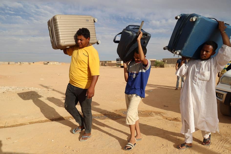 Three people carry suitcases after fleeing their home in Sudan 