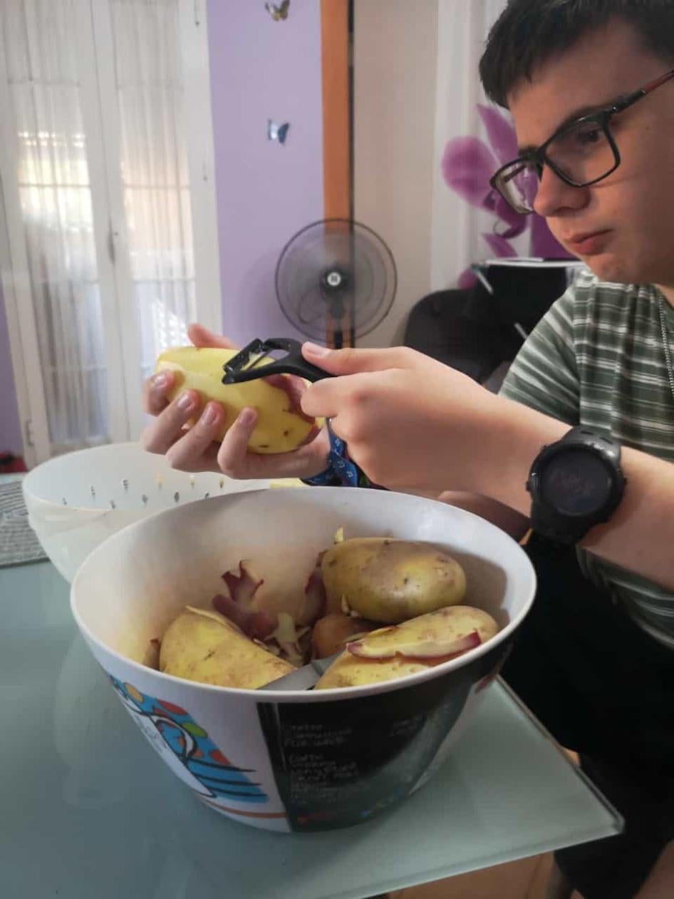 Abraham Osorio, de 13 años, quien tiene autismo, ayuda a su madre a pelar patatas junto a un ventilador eléctrico para mantenerse fresco en su vivienda en Sevilla (Andalucía, España).