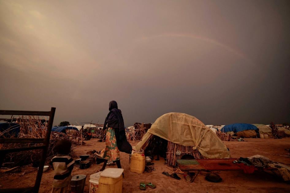 A woman stands by a tent in a refugee camp