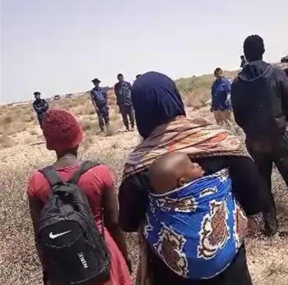 Un groupe de migrant·e·s et de demandeur·euse·s d’asile noir·e·s de plusieurs nationalités africaines, dont une femme et son bébé, bloqué·e·s dans le désert depuis des jours après avoir été expulsé·e·s de Tunisie, debout dans la zone tampon à la frontière entre la Tunisie et la Libye, face à une équipe de journalistes d’Al Jazeera et à des soldats libyens, le 11 juillet 2023. © 2023 Privé