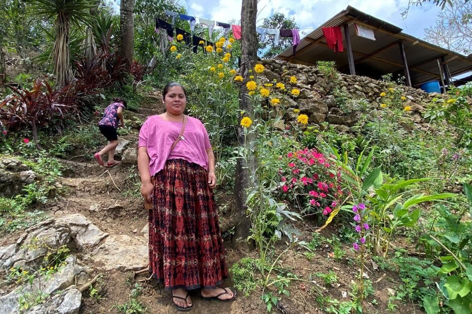 A woman stands in front of her home on a mountainside
