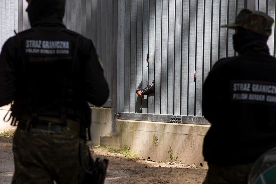 border guards watch asylum seekers stuck behind a border wall 