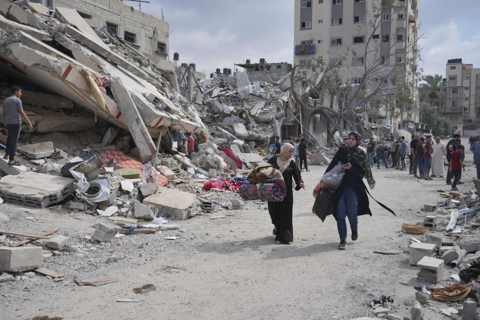 נשים פלסטיניות חולפות על פני בניינים שנחרבו בתקיפות אוויריות של ישראל במחנה הפליטים א-נוסייראת במרכז רצועת עזה, 16 באוקטובר 2023.