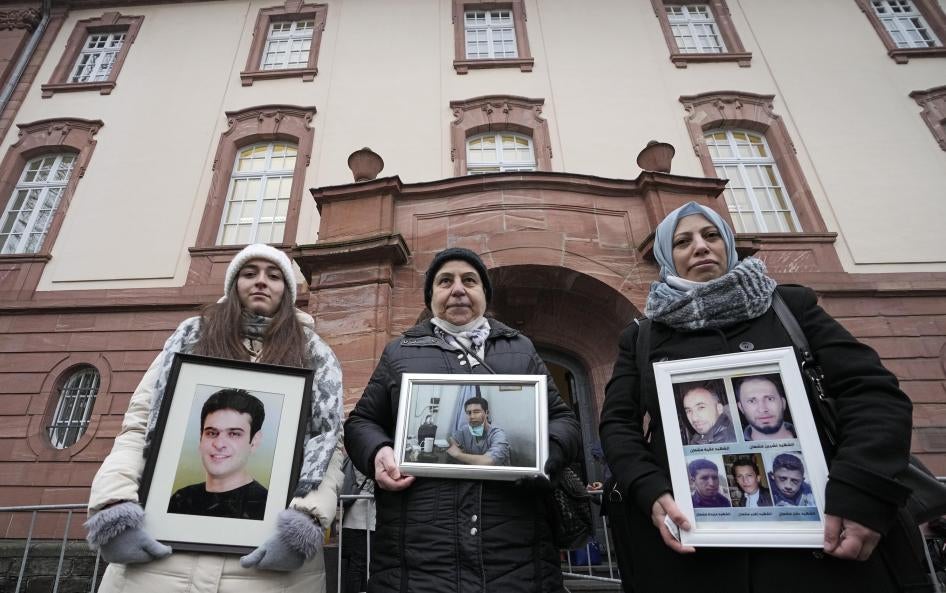 Women hold photos of relatives who died in Syria in front of a court in Koblenz, Germany, January 13, 2022. 