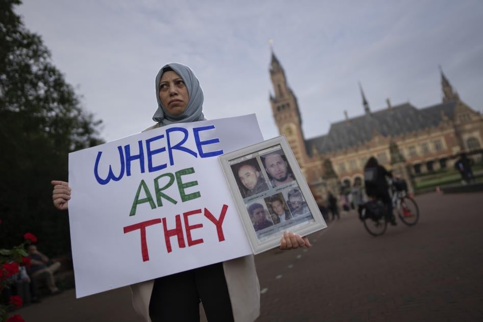 A protester stands in front of the International Court of Justice holding pictures of people she said were disappeared in Syria, The Hague, Netherlands, October 10, 2023. 