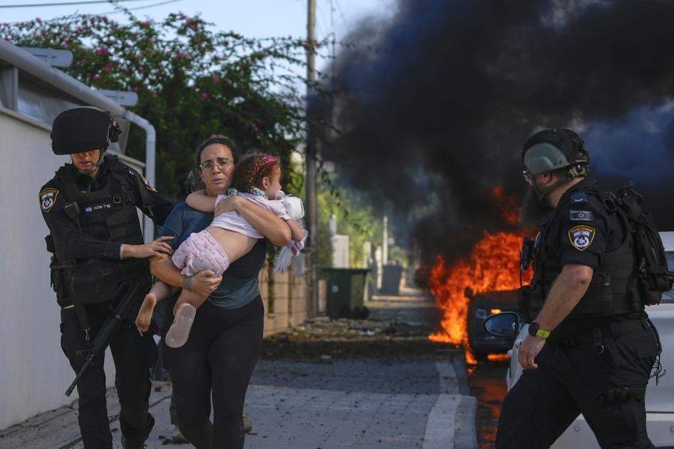 Police officers evacuate a woman and a child from a site hit by a rocket fired from the Gaza Strip, in Ashkelon, southern Israel, on October 7, 2023.