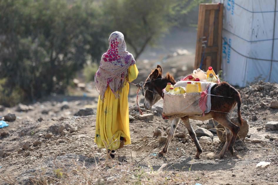 A girl walks with a donkey carrying water containers