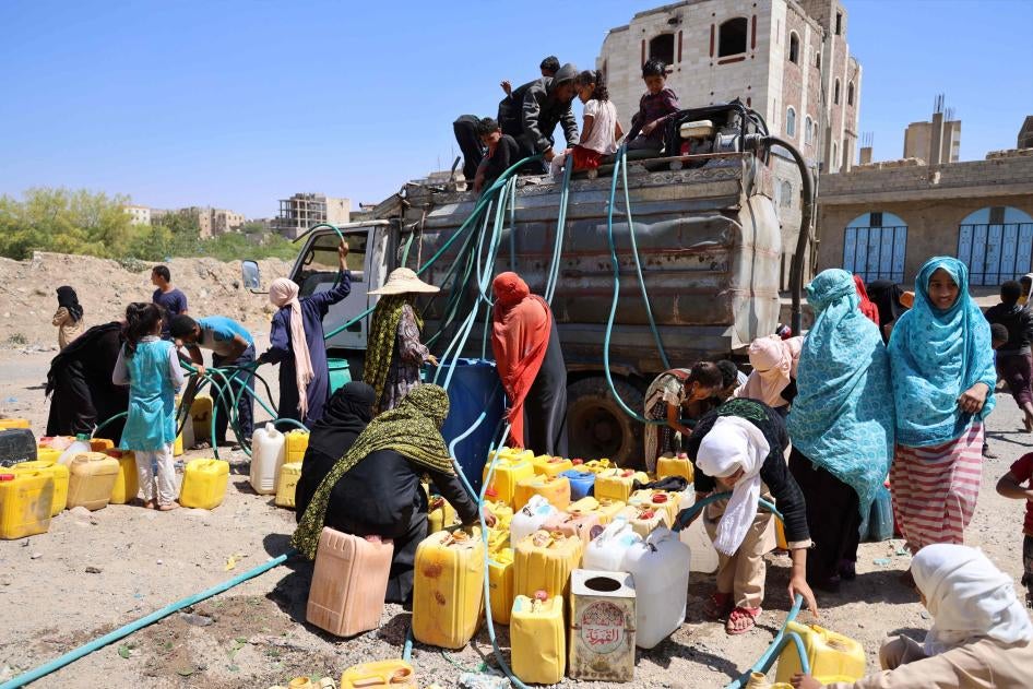 A group of women and children get water from a water truck